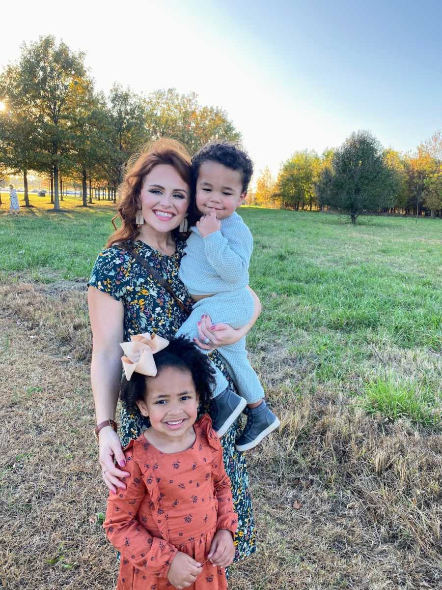 Mother holding son and daughter standing in front of her outside