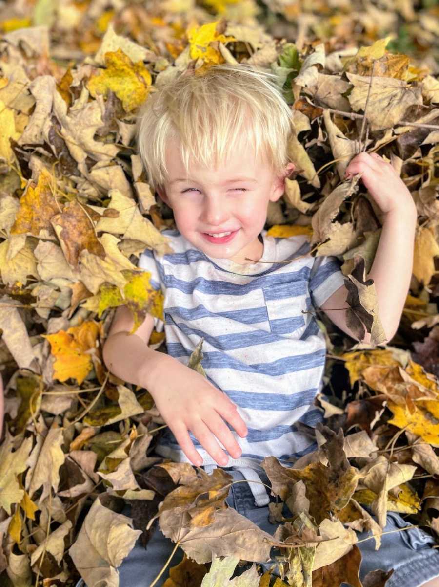 Young boy lying in pile of leaves