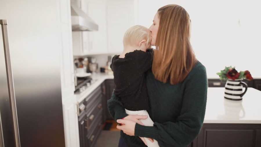 Mom holding baby son in kitchen kissing him on head