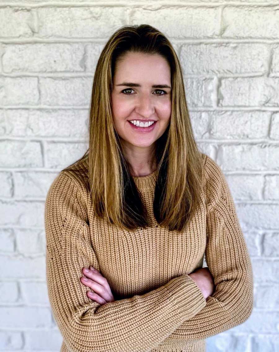 Woman standing with arms crossed in front of white brick wall