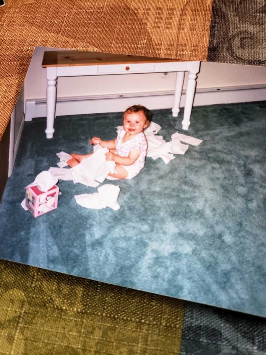 Baby girl sitting on blue carpet playing with tissues