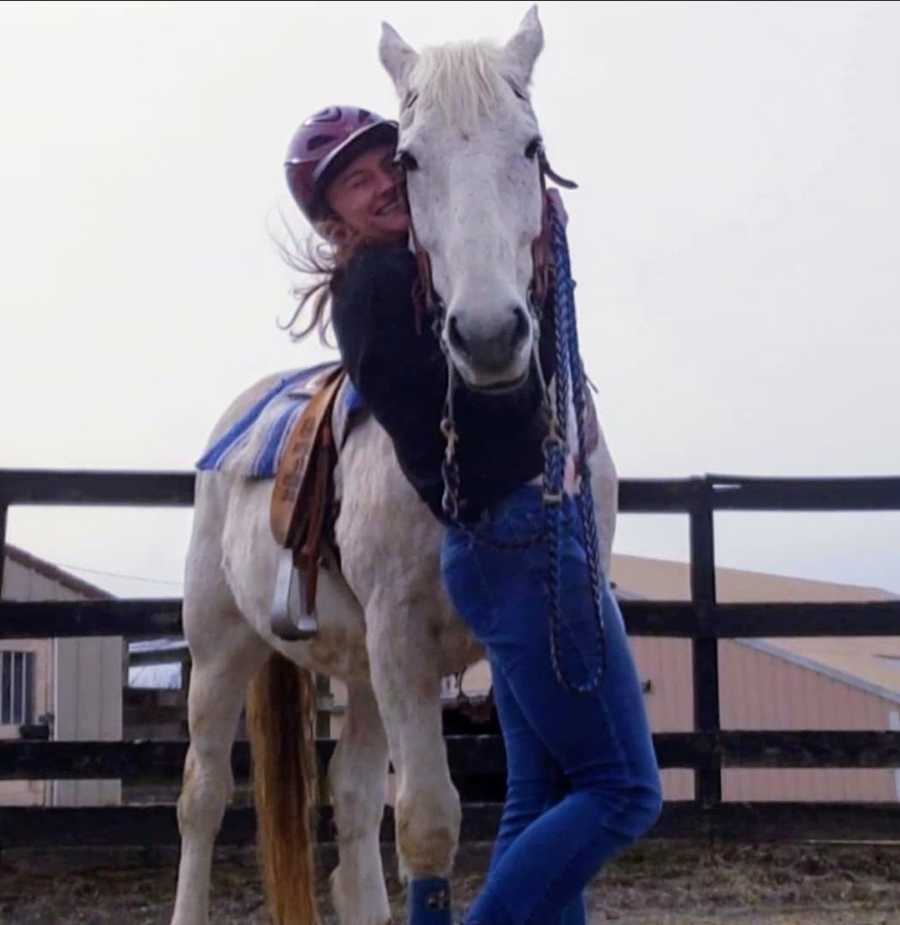 Woman wearing riding helmet hugging white horse