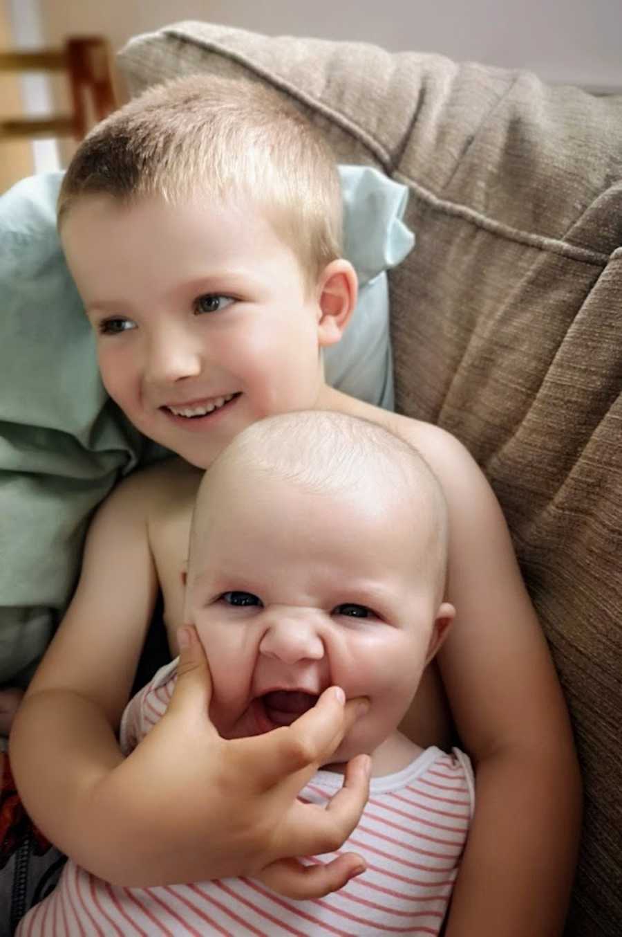 Big brother holding baby brother and squishing his cheeks 