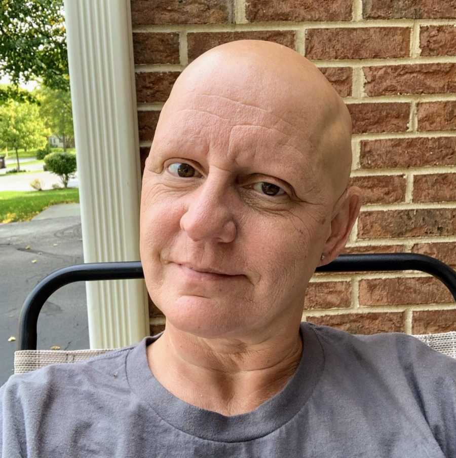 Bald woman taking selfie in front of brick wall