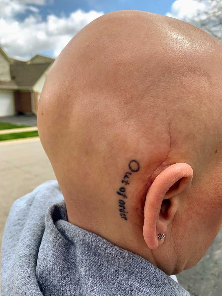 Bald woman showing off hearing aid and behind-the-ear tattoo