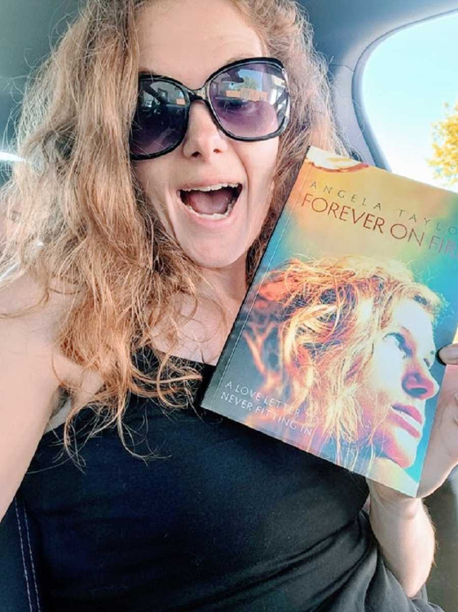 A neurodivergent woman holds up her book in the car