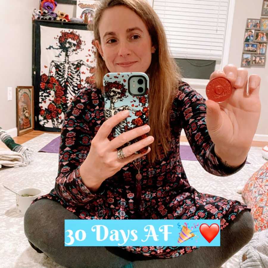 A woman holds up her 30 days sober chip from AA