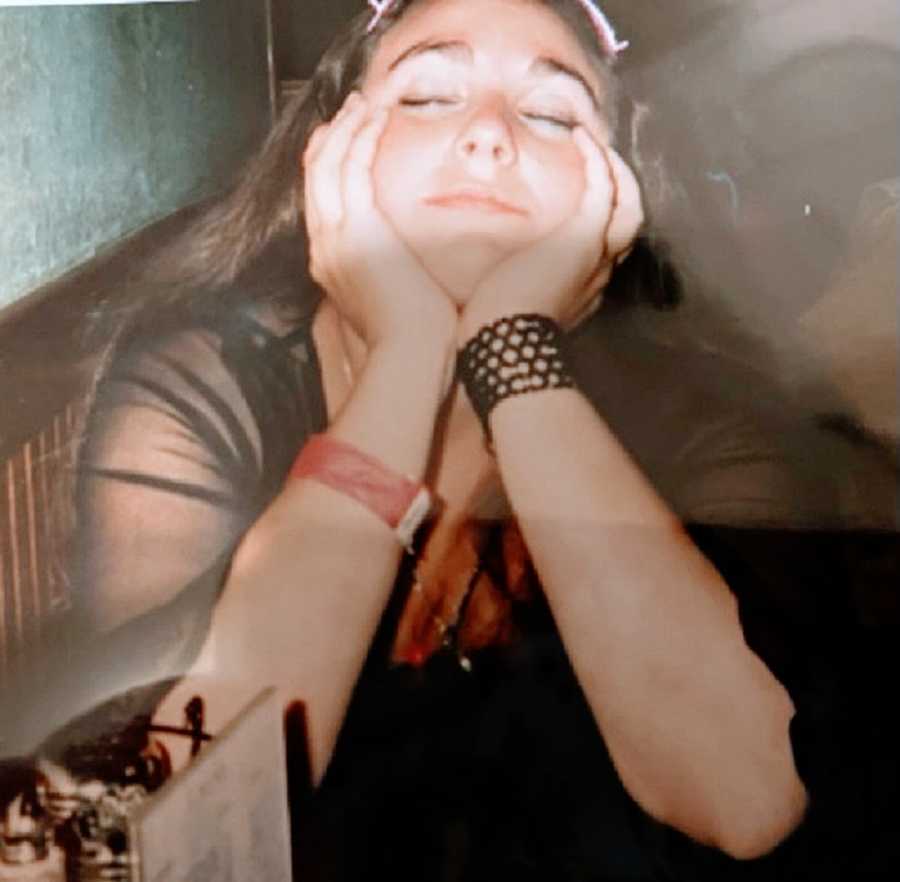 A young woman sits with her eyes closed and hands on her face