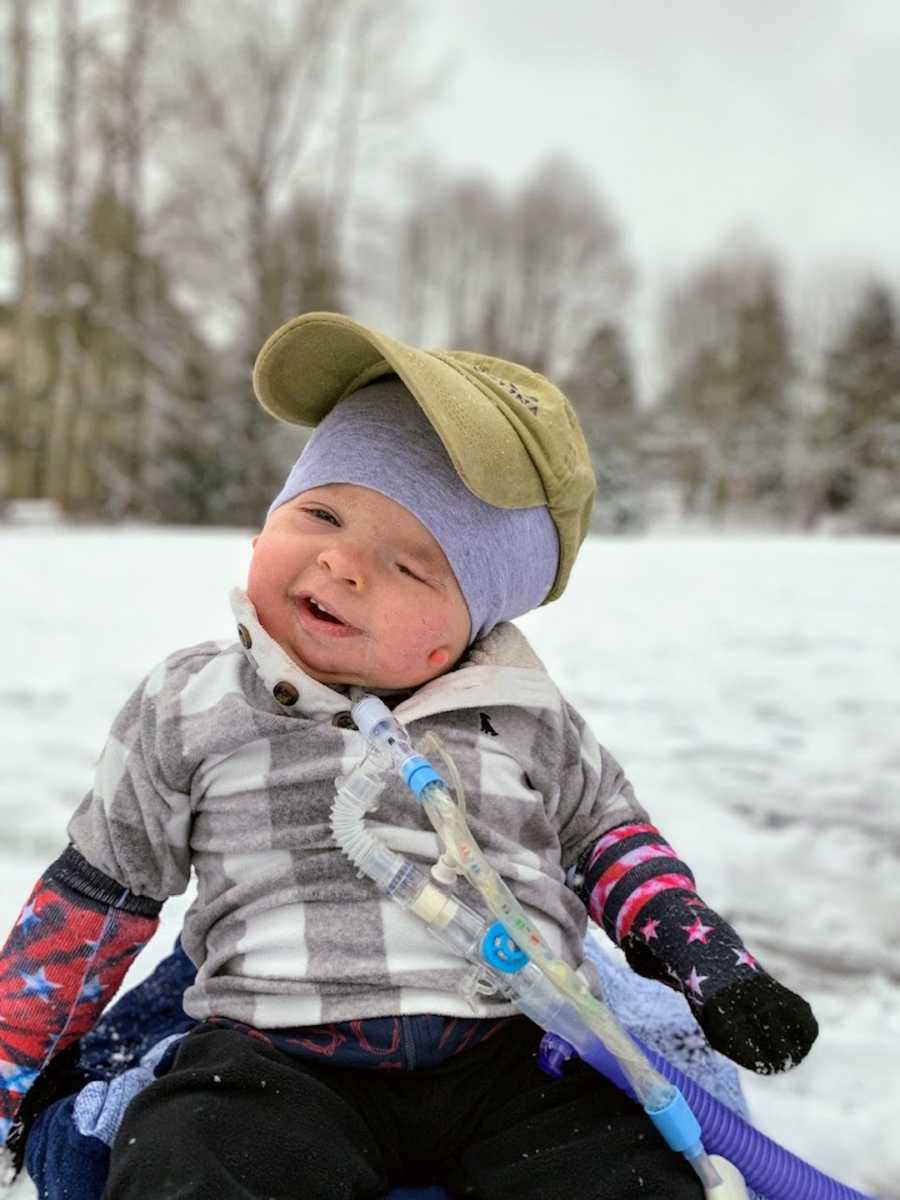 Baby boy wearing hat and smiling sitting outside in snow