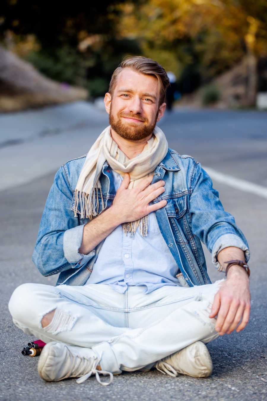 Man sitting cross-legged in the road with hand on heart smiling