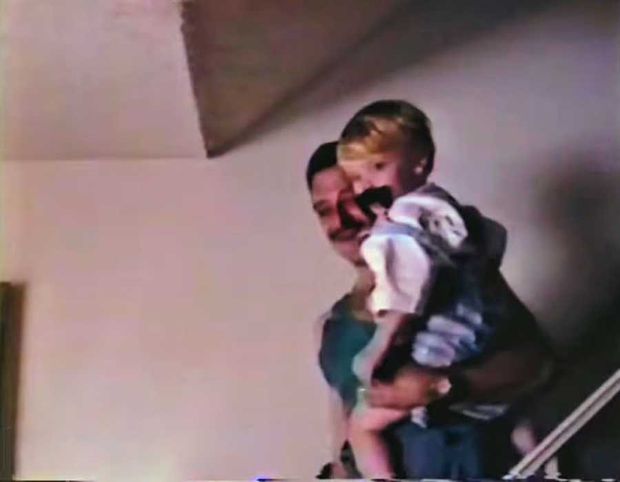 Father holding son on staircase, the son is wearing a fake moustache 