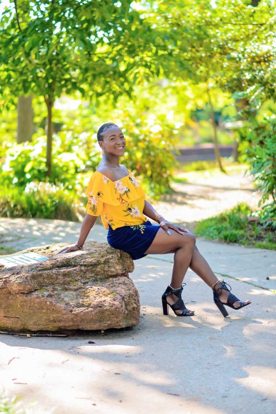 A woman wearing yellow sits on a rock in the park