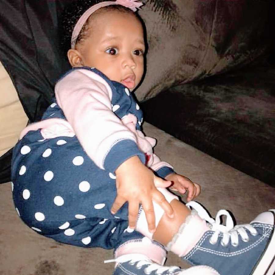 A little girl wearing a polka-dotted outfit sits on a couch