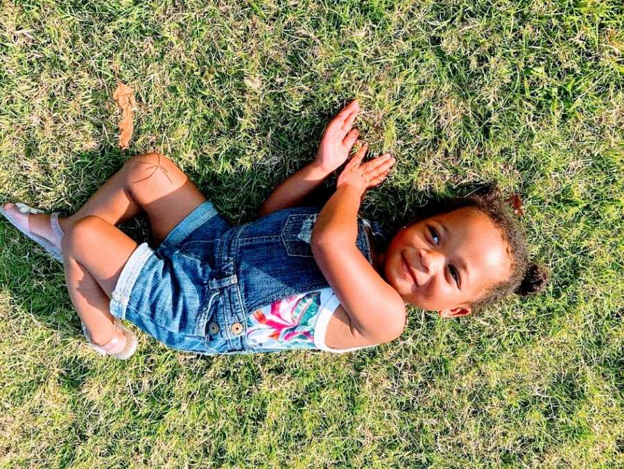 A little girl lies on her side in the grass