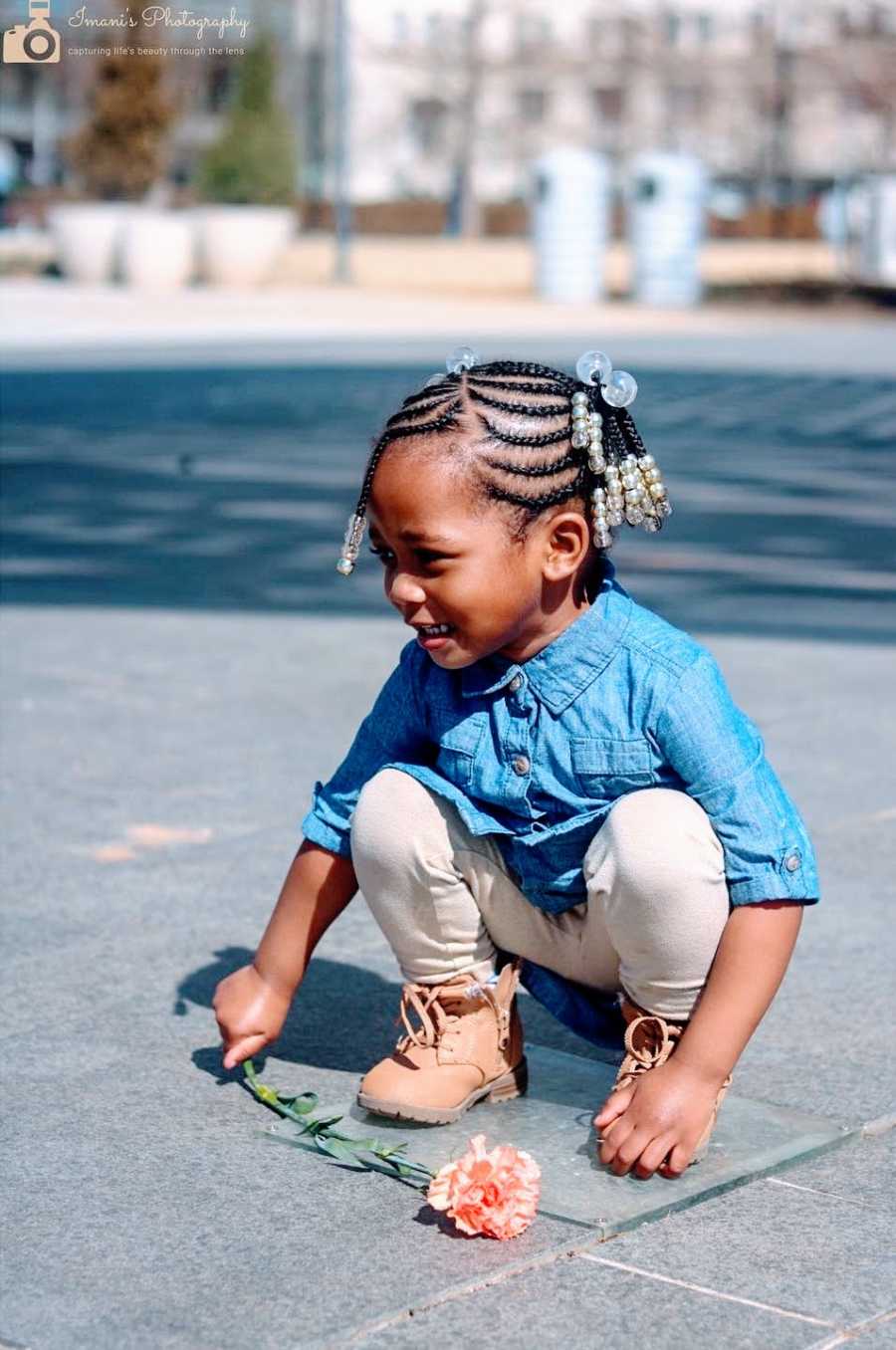 A little girl squats down holding a flower in her hand