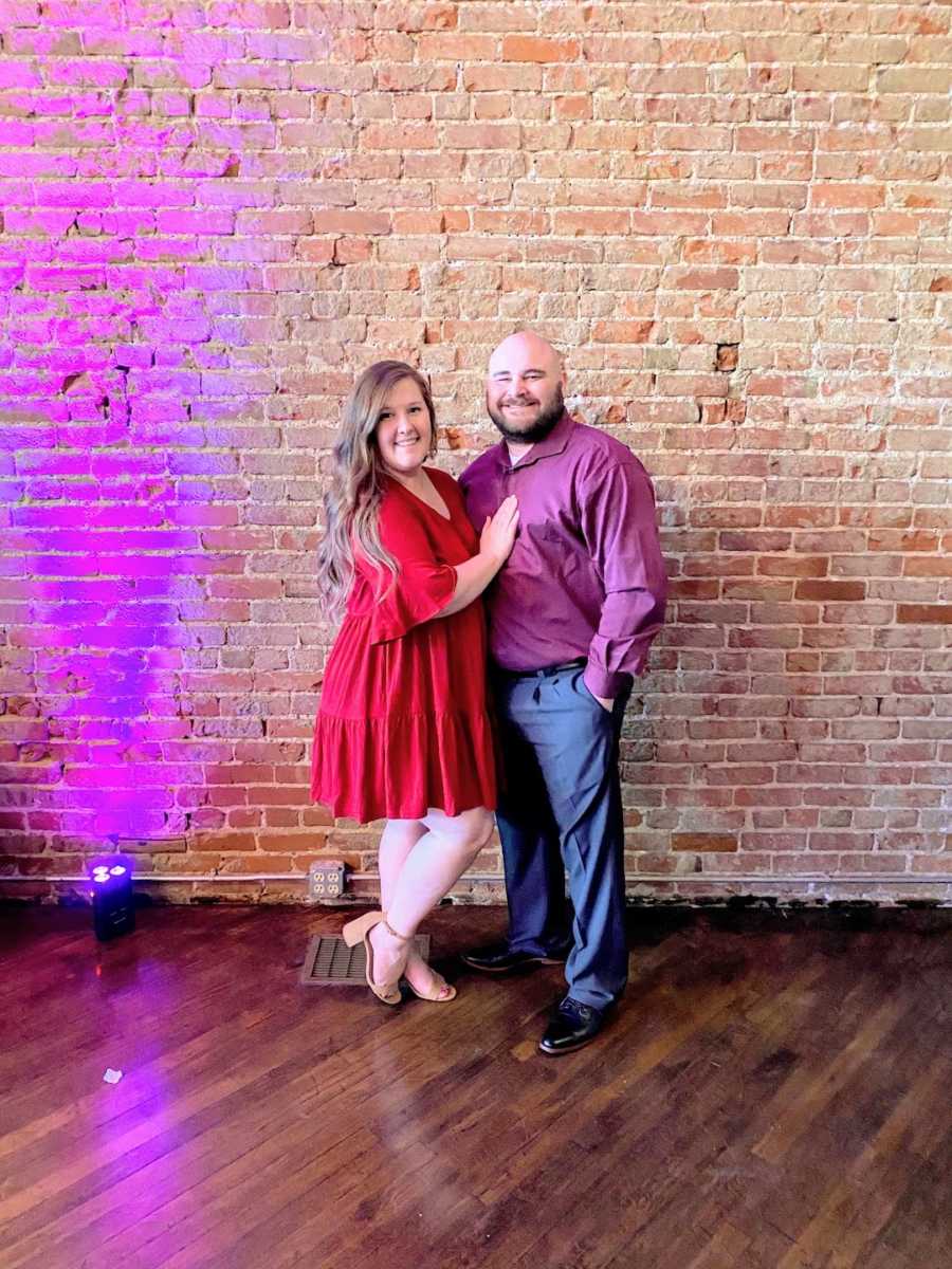 Couple standing and smiling in front of brick wall