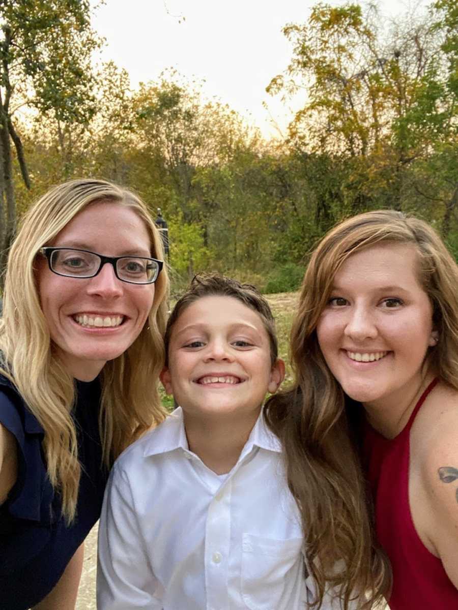 Two moms smiling with son outside by trees