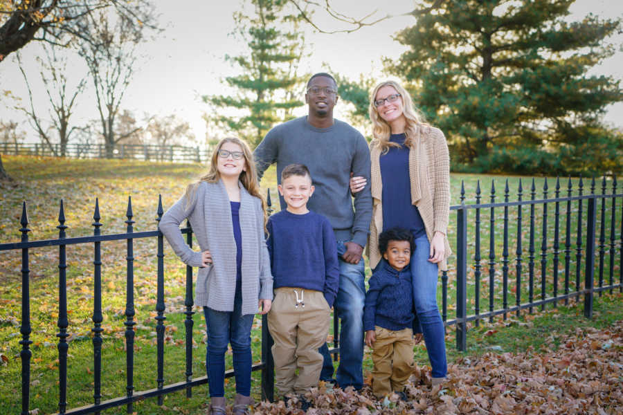 Family of five standing by black fence outside smiling