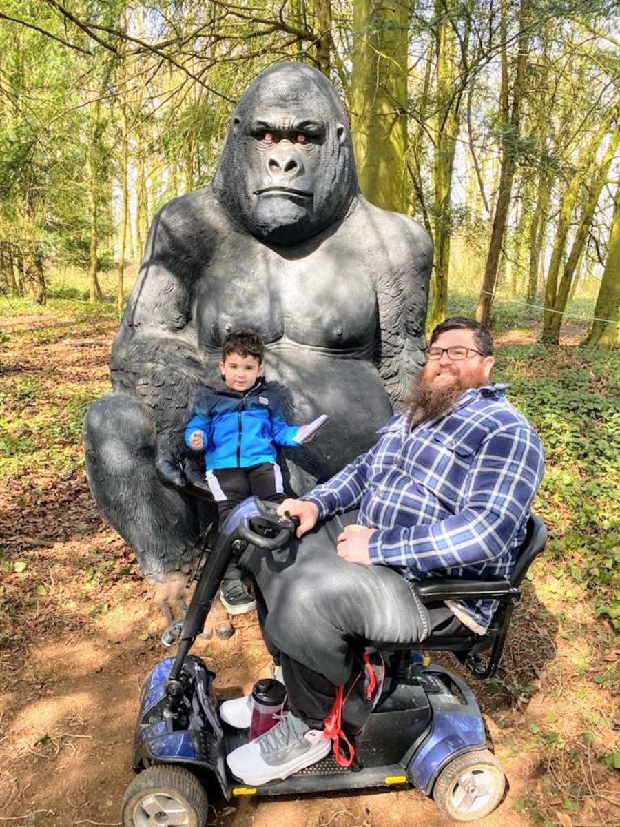 Man in wheelchair posing with son in front of gorilla statue