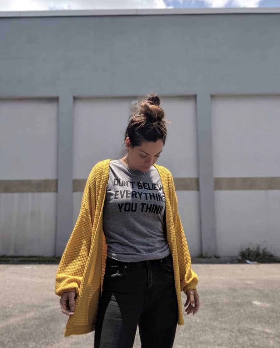 Woman looking down at shirt standing outside wearing yellow sweater