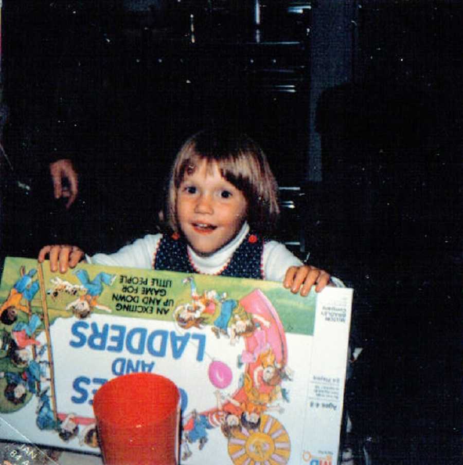 A young girl with autism and ADHD holds a Chutes and Ladders board game