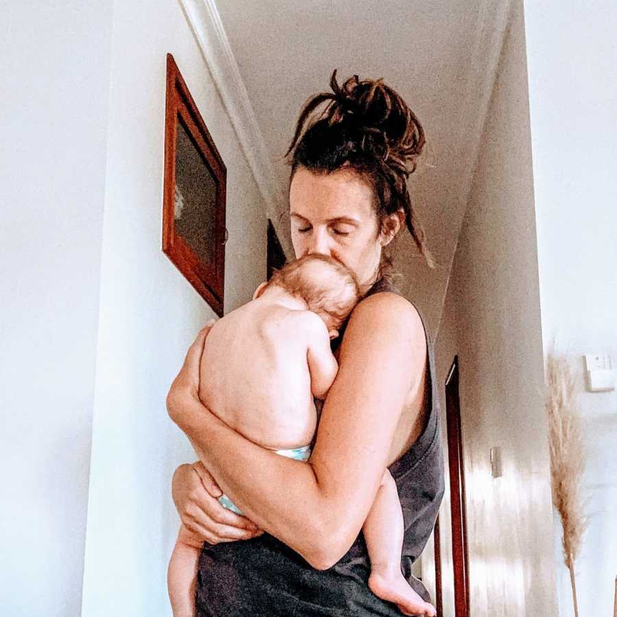 A mother holds her baby while standing with messy hair