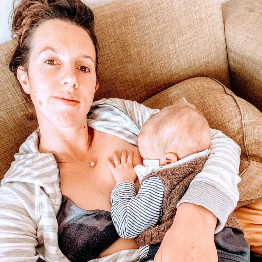 A mother cradles her baby to her chest on a couch