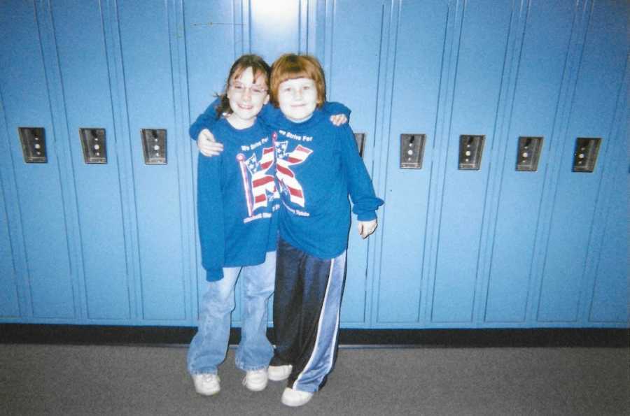 Old photo of two young girls wearing matching sweatshirts standing in front of blue lockers