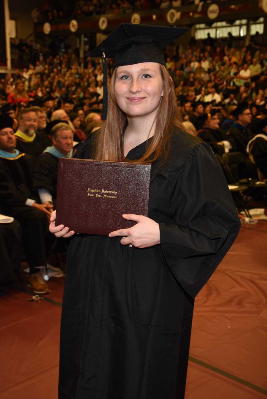 College graduate wearing cap and gown and holding diploma at graduation