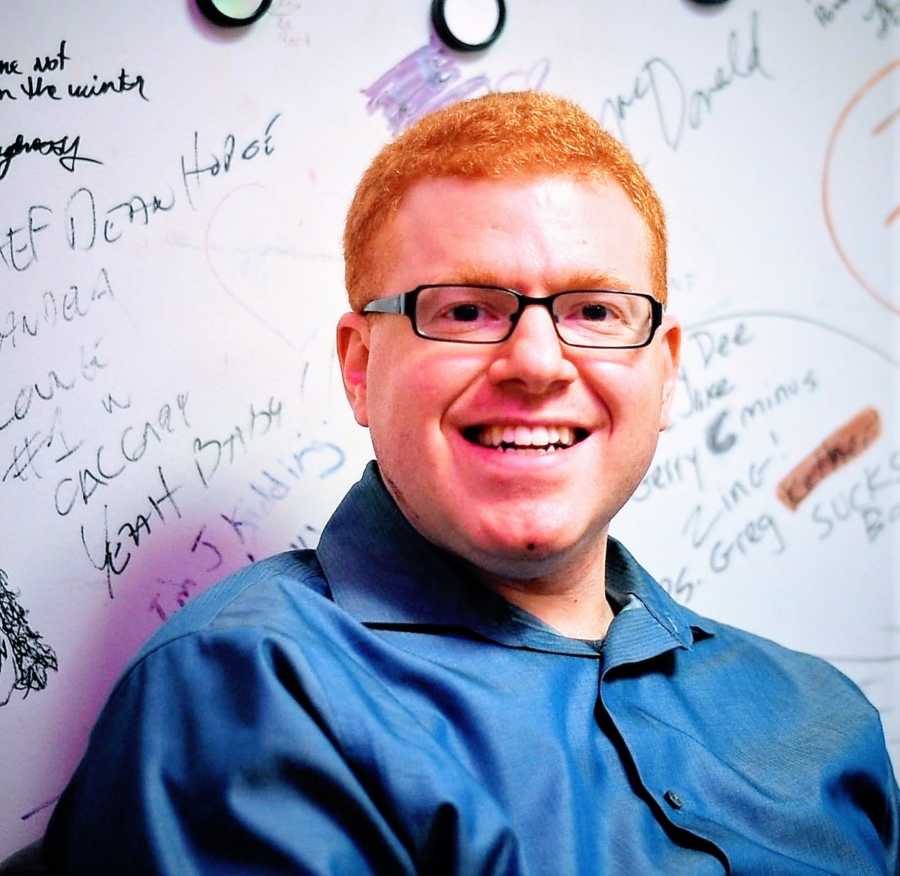 A comedian stands in front of a whiteboard with writing on it