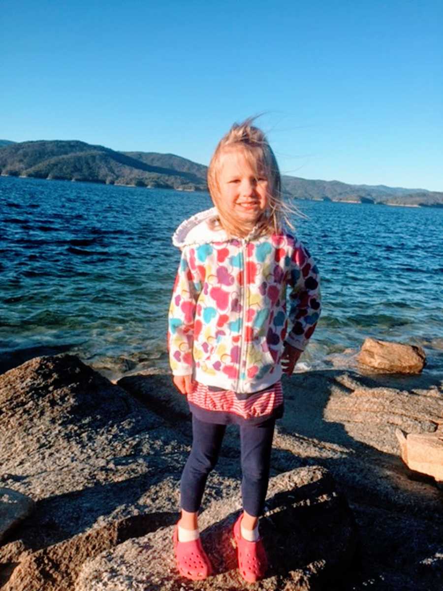 A young adopted girl stands on rocks by the water