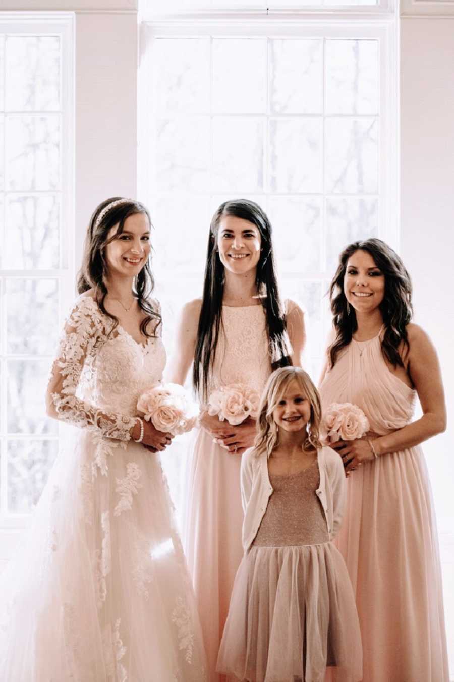 A bride and her sisters stand together wearing dresses