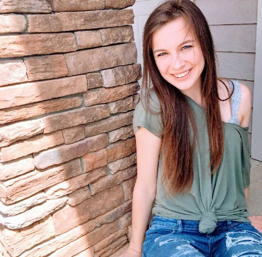 A young woman sits outside by a wall of stone