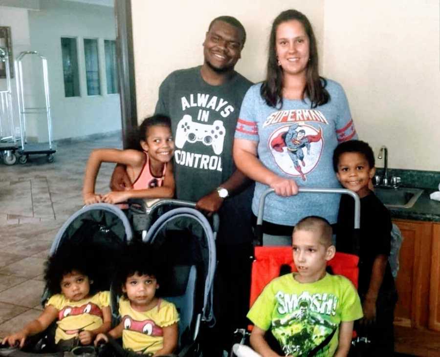 A boy sits in a stroller with his four siblings and parents near him