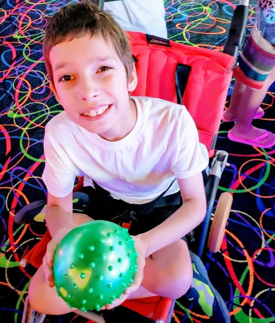 A boy with Ring14 sits in his stroller at am arcade holding a green ball