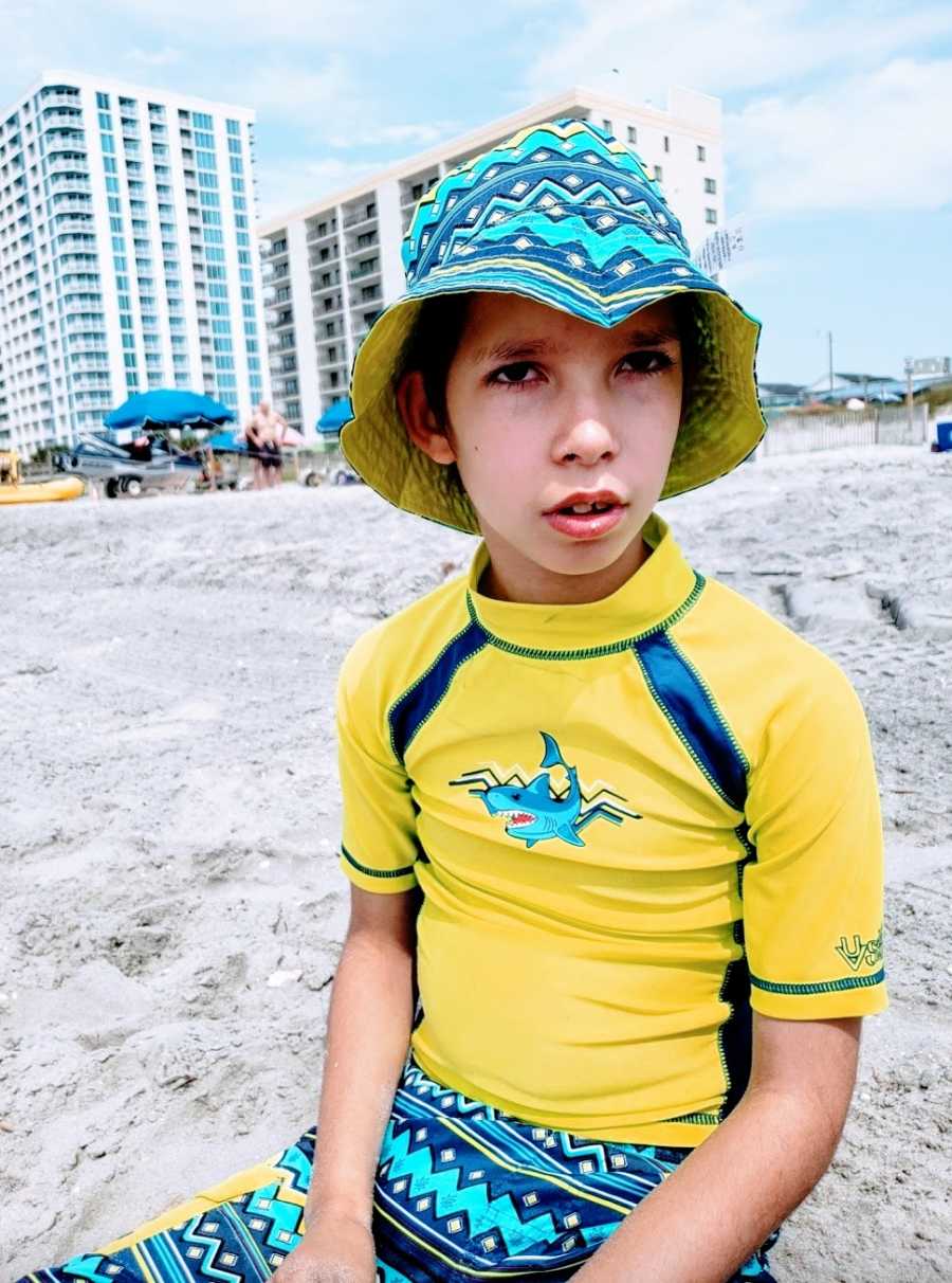 A boy with a rare chromosome condition wearing a yellow swimshirt at the beach