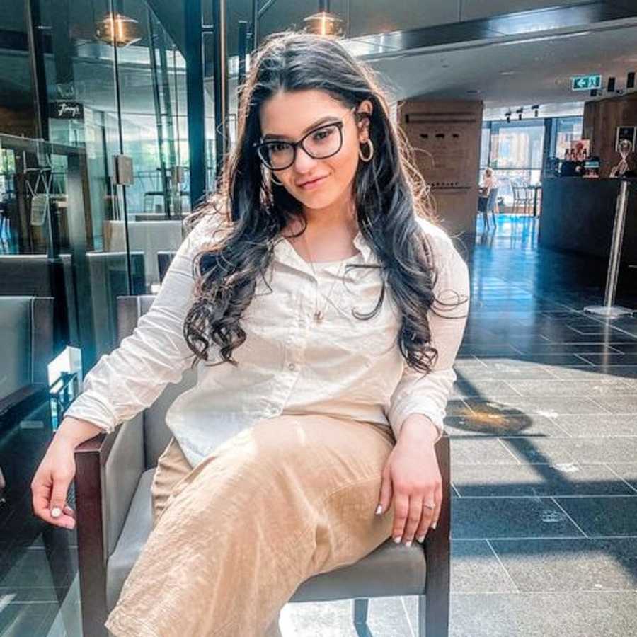 A woman with ADHD sits in a tall chair wearing glasses and a white shirt