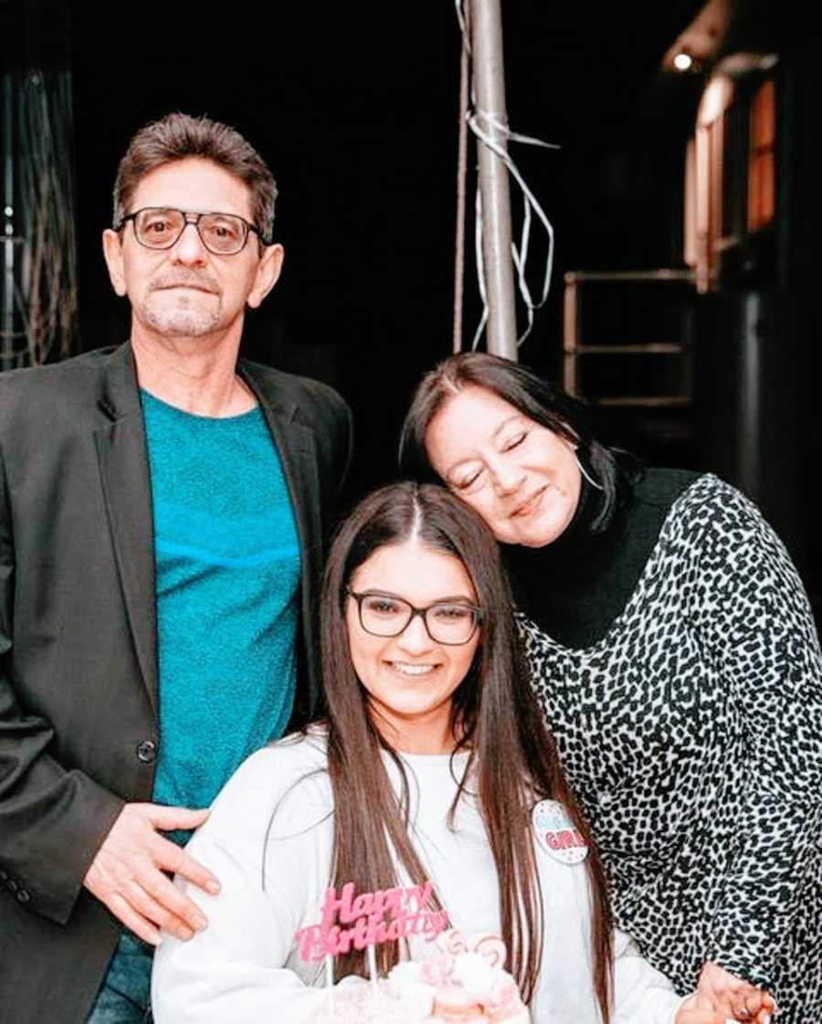 A woman with ADHD sits between her parents holding a birthday cake