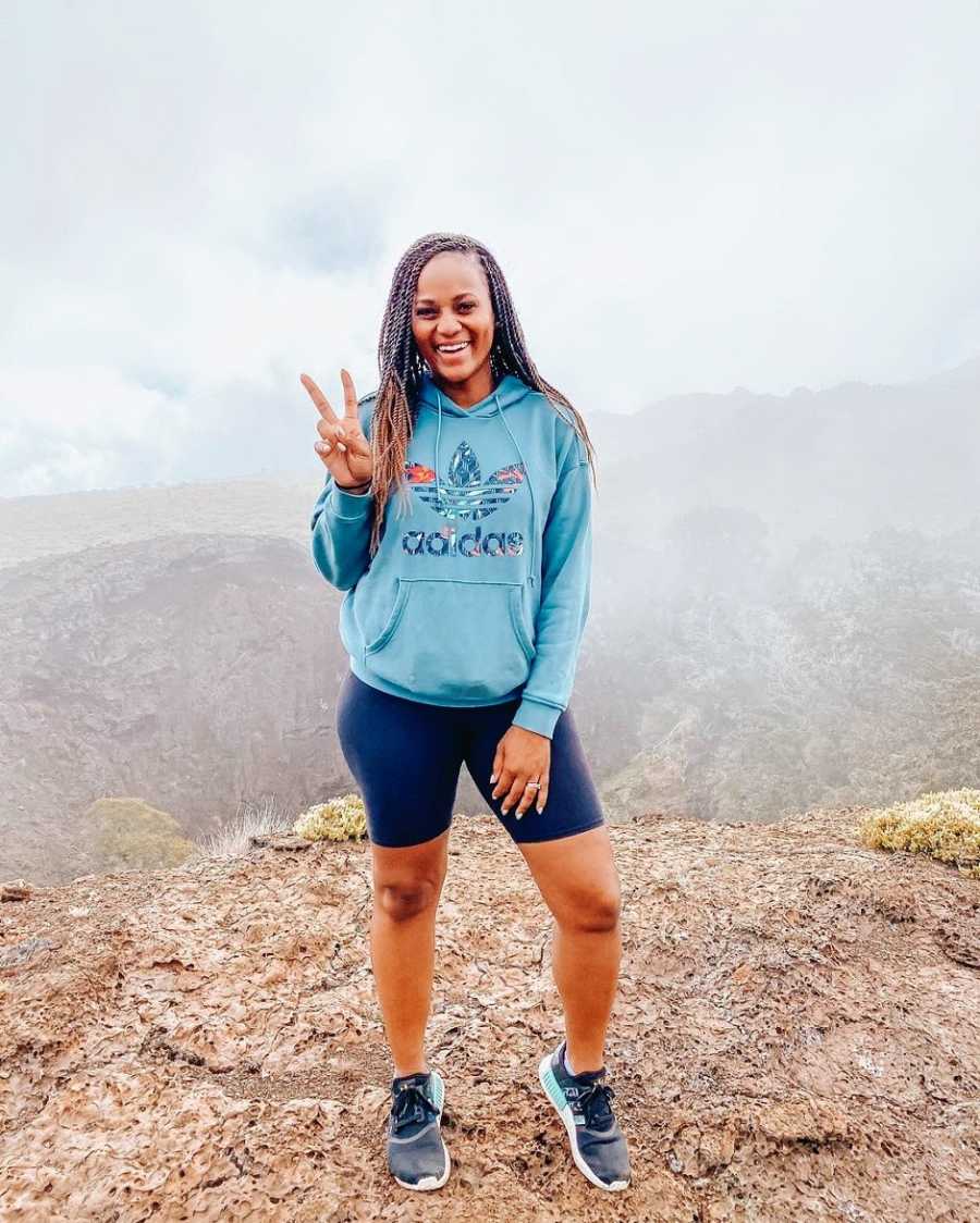 A woman in a blue hoodie making a peace sign on a volcano 