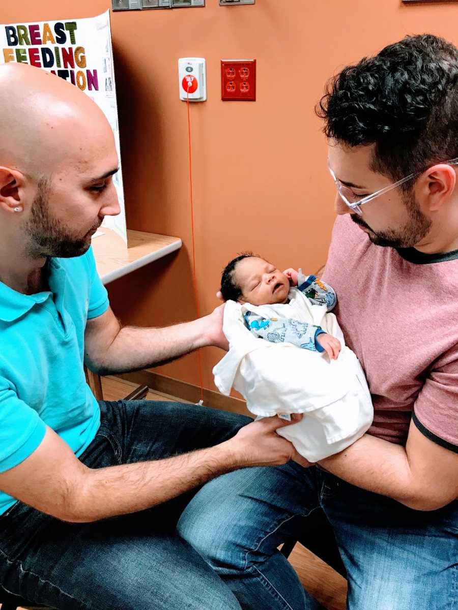 Gay fathers hold their newborn son in a hospital