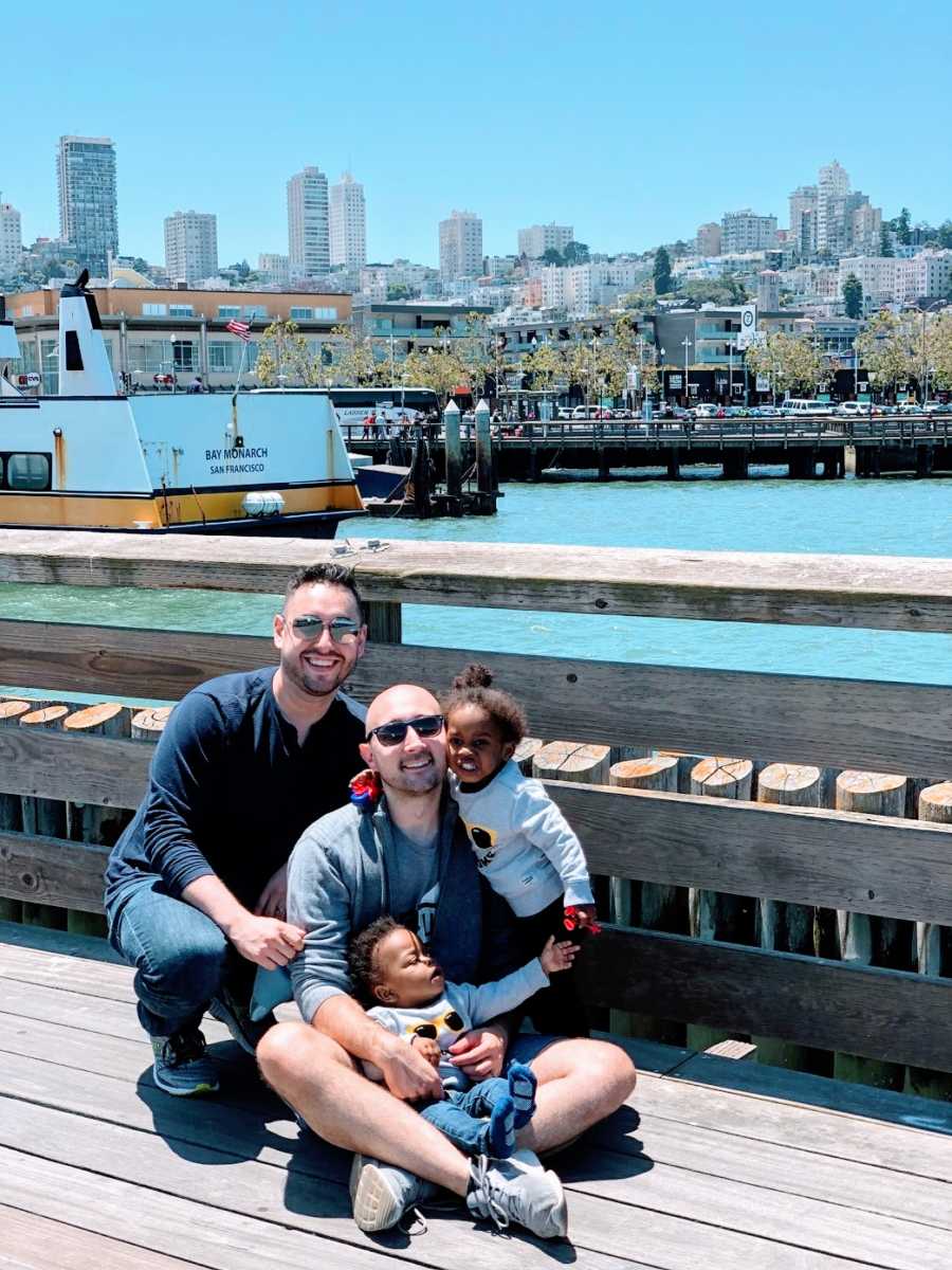 Gay fathers with their adopted toddlers at a fence by the water