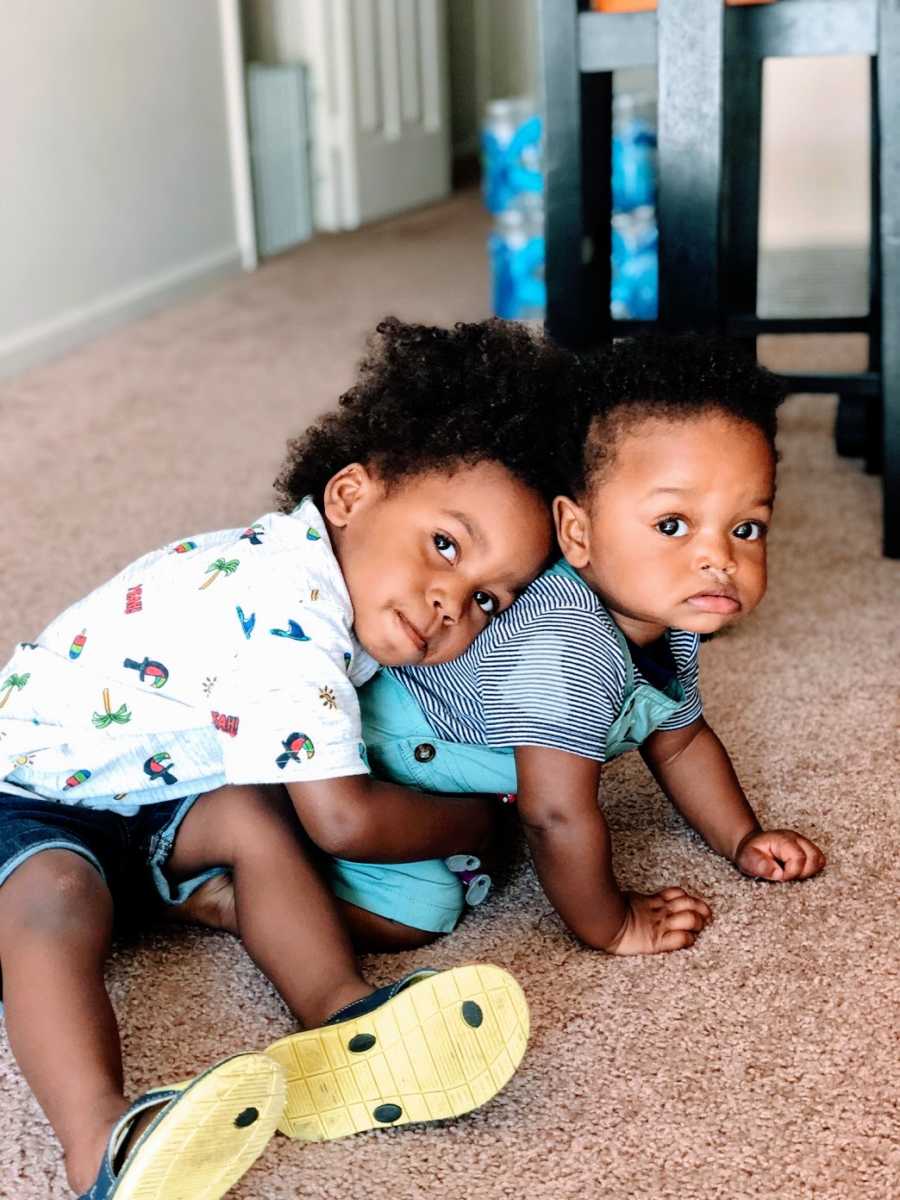 A toddler hugs his baby brother, who is trying to crawl away