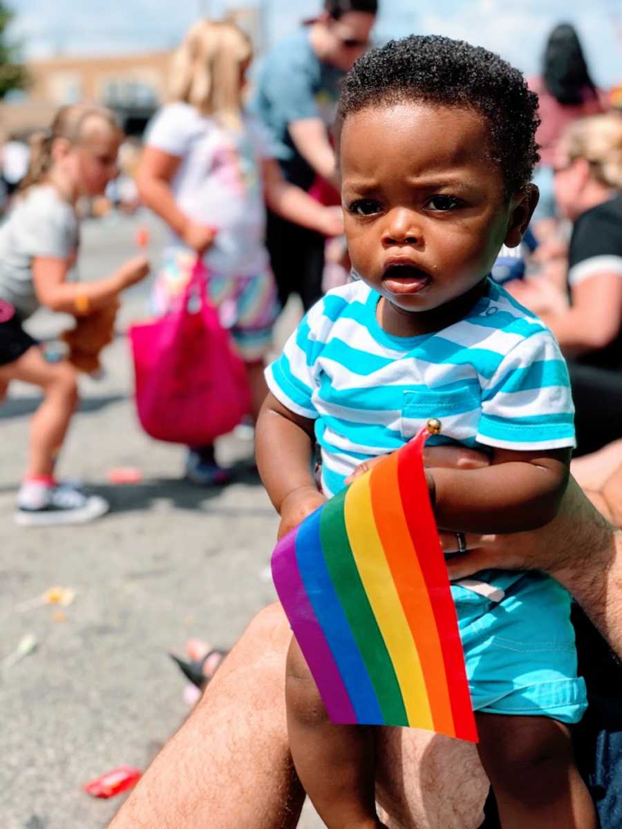 A baby boy holds a pride flag outdoors