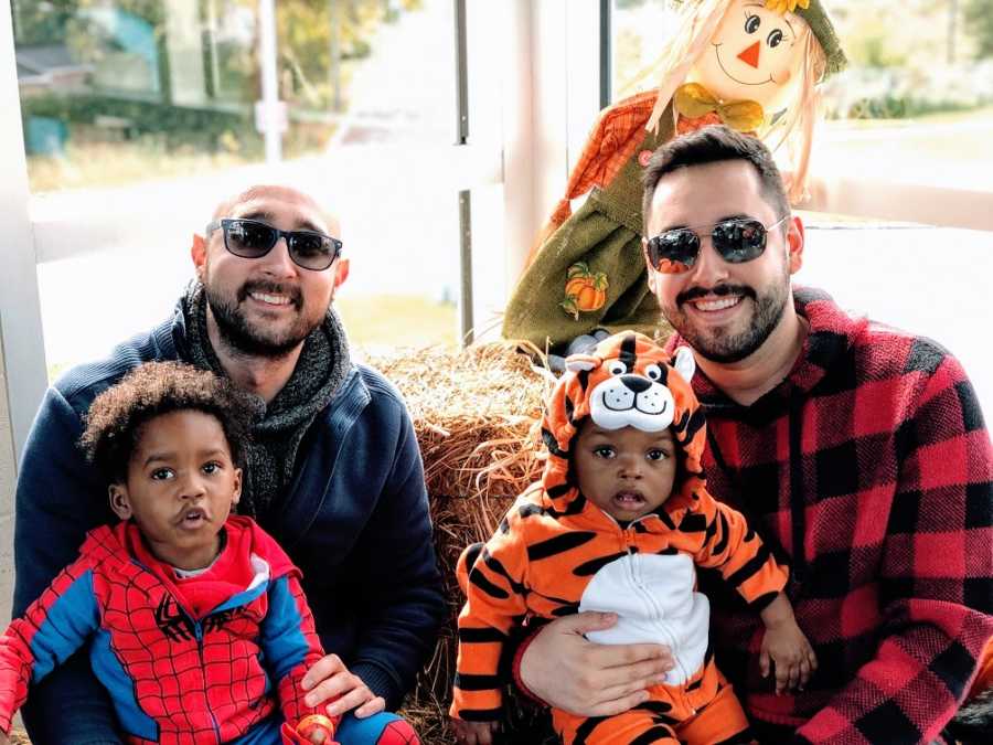 Gay fathers hold their adoptive sons who are wearing Halloween costumes