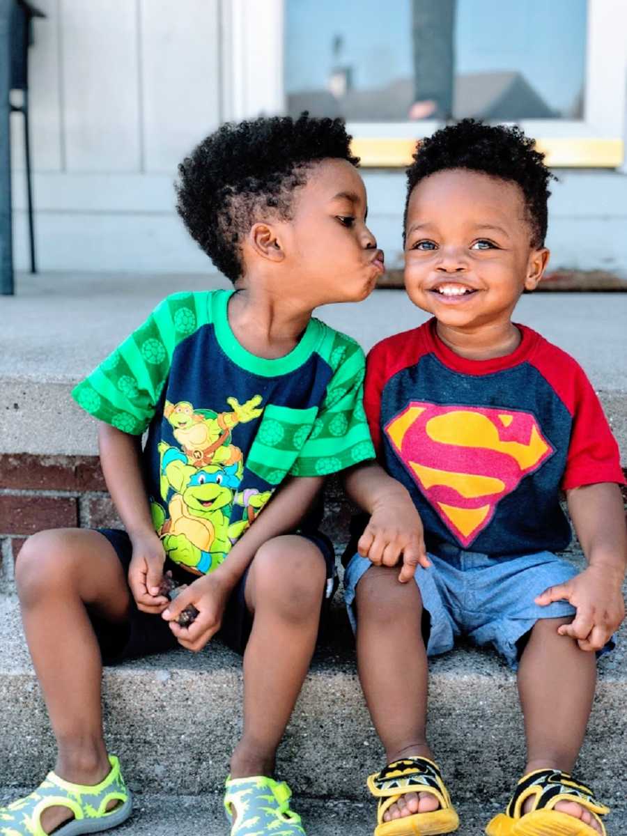 A boy leans over to kiss his younger brother on the cheek