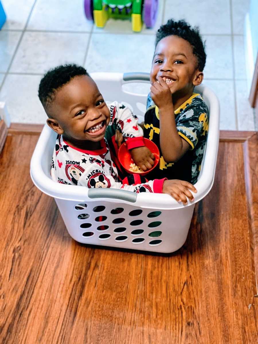 A pair of brothers sit smiling in a laundry basket