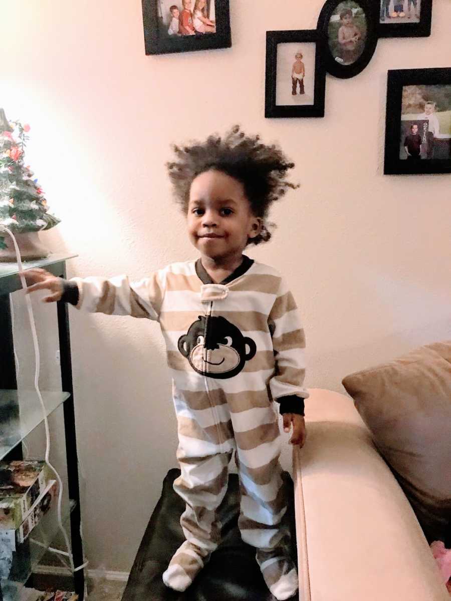 A toddler wearing pajamas stands next to Christmas decorations