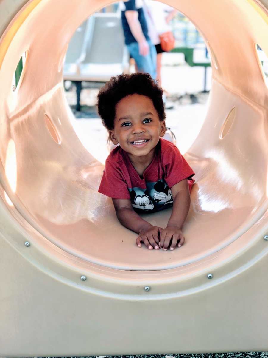 A boy in a red Mickey Mouse shirt plays in a plastic tunnel