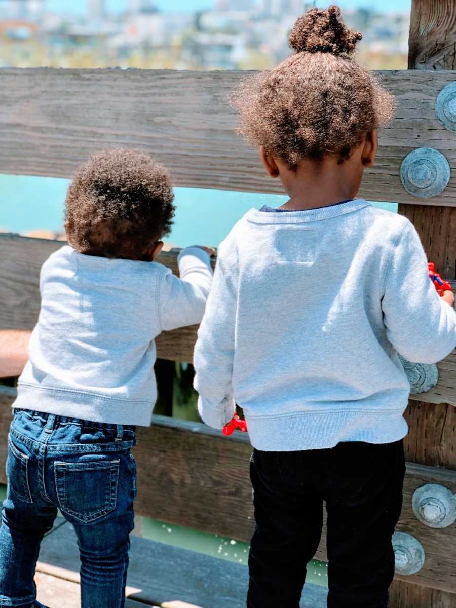 Brothers wearing grey sweaters look at the water through a fence