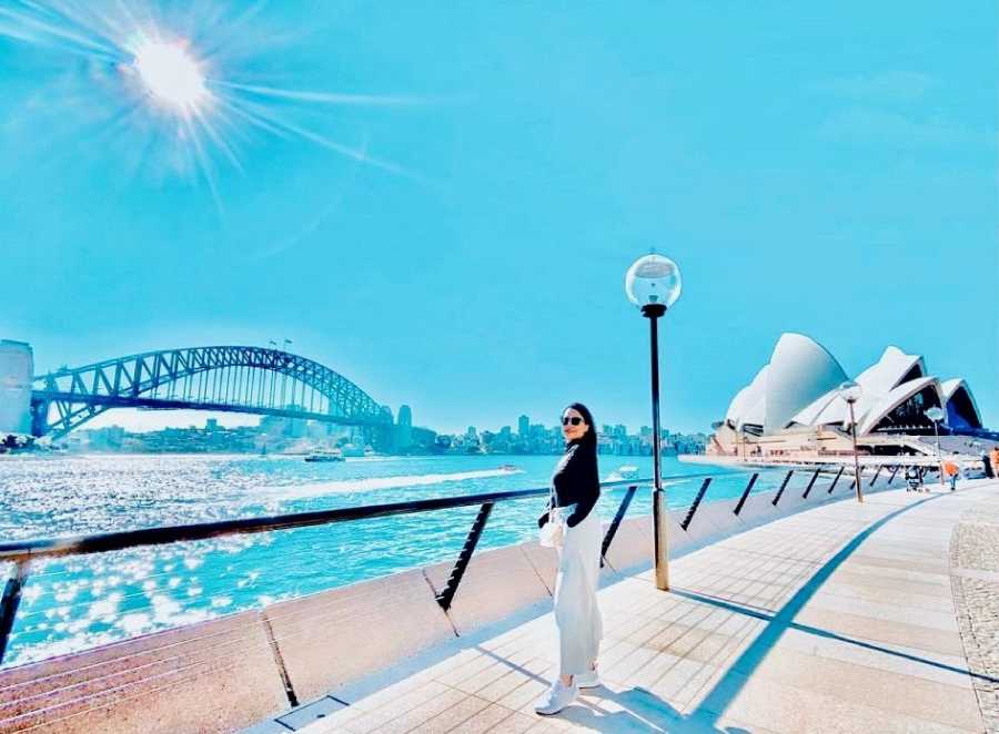 A single mother with alopecia stands on a bridge in front of the Sydney Opera House
